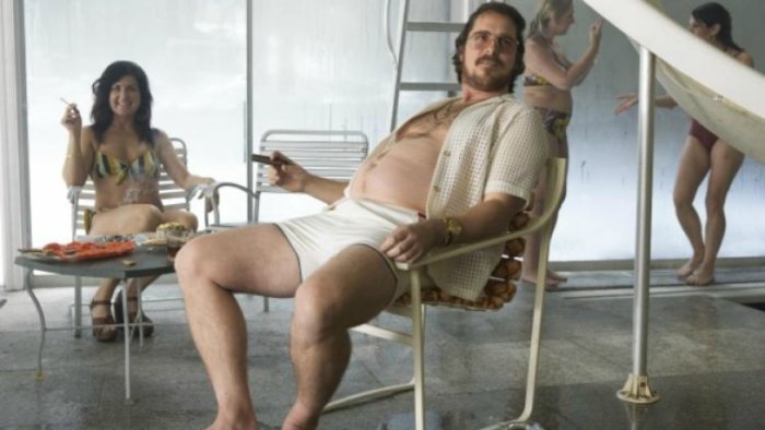 Christian Bale sat in a chair in American Hustle