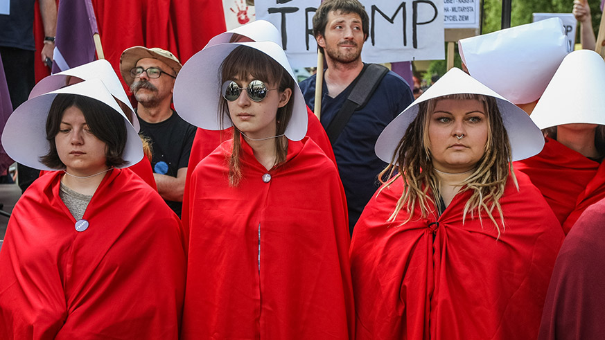 Women dressed as handmaids protest against Trump’s visit to Poland