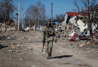 Ukrainian service member walks in a destroyed village on the front line in the east Kyiv region