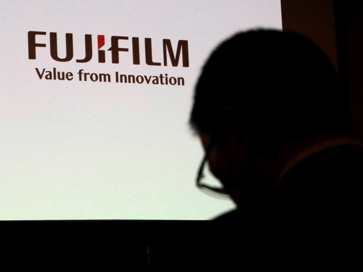 A man is silhouetted in front of Fujifilm Holdings’ logo