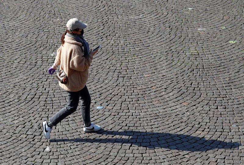 A woman wearing a mask crosses an empty square in