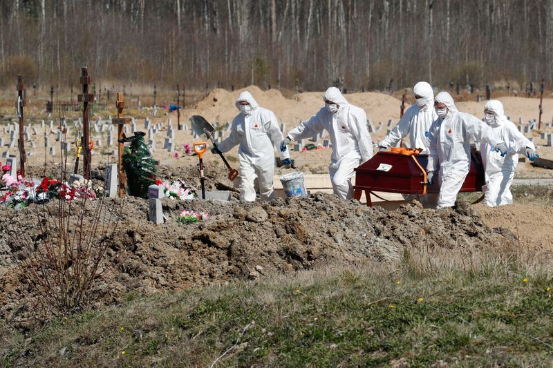 Grave diggers bury a coronavirus disease victim at a graveyard