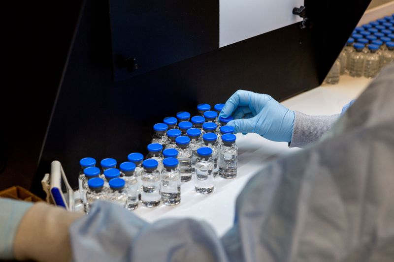 A lab technician inspects filled vials of investigational remdesivir at