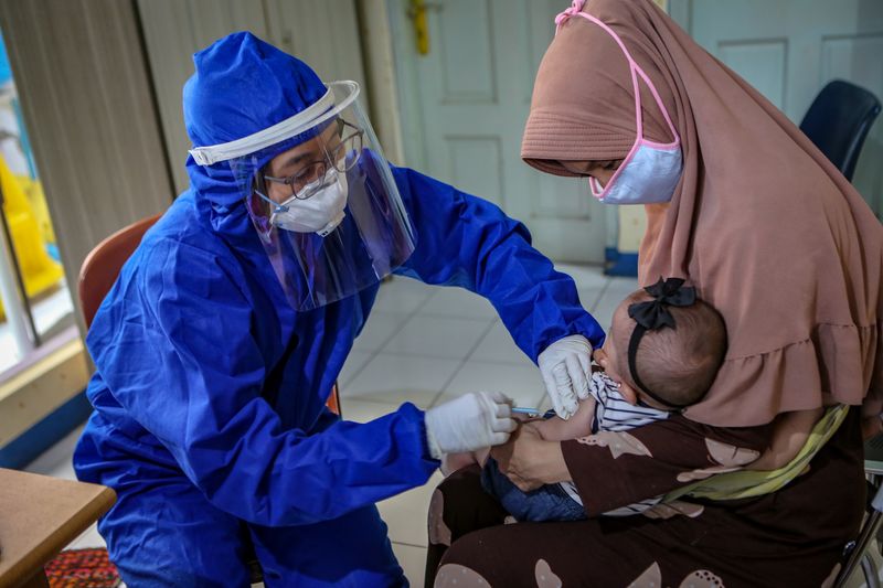 A medical staff member wearing PPE vaccinates a baby in