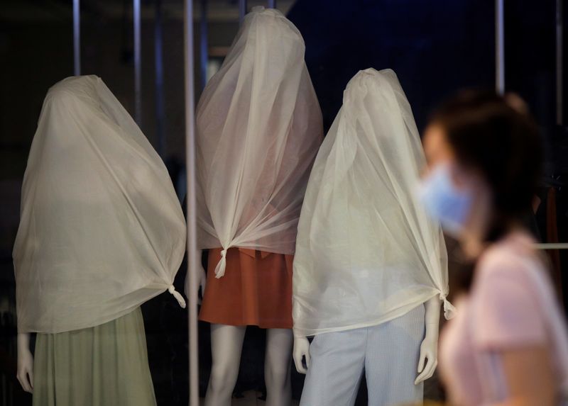 A woman wearing a protective face mask passes covered mannequins