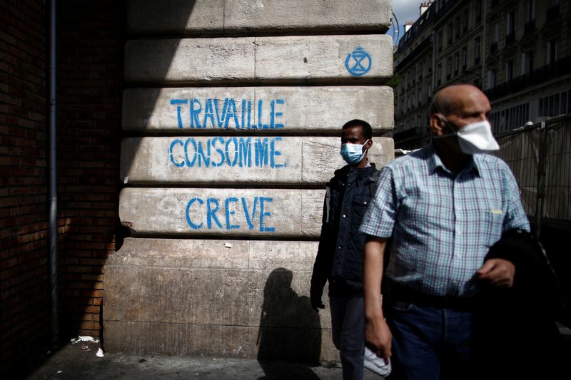 People wearing protective face masks walk past the slogan which