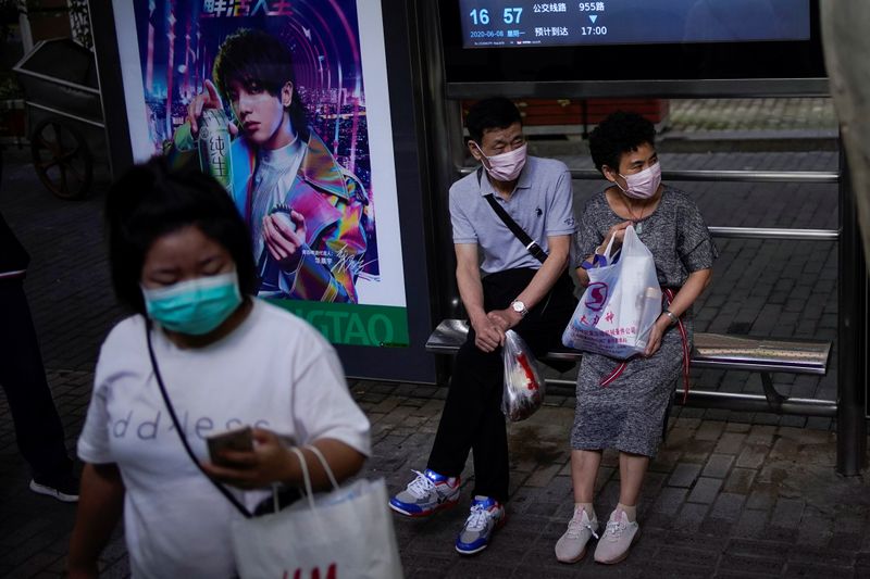 FILE PHOTO: People wearing face masks wait for a bus
