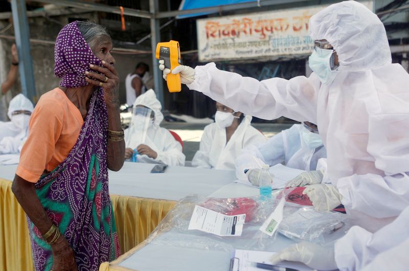 A health-worker wearing personal protective equipment (PPE) checks the temperature