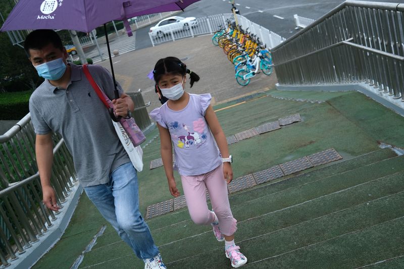 Man holds an umbrella for a girl, both wearing face