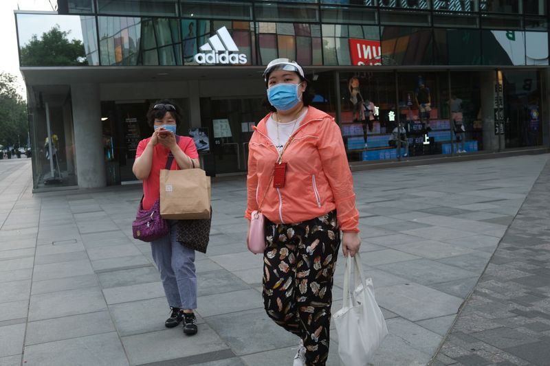 Woman wearing a face mask walks past a Adidas store