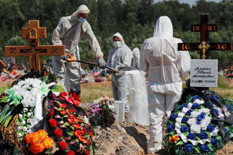Grave diggers wearing personal protective equipment bury a person on