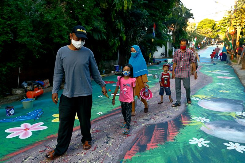 People wearing protective face masks walk past a mural depicting