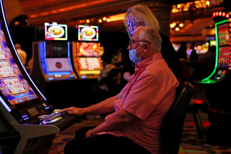 FILE PHOTO: People wearing protective face masks play slot machines