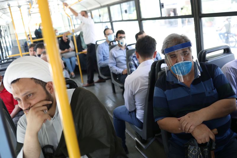 Iranians wearing protective masks and face shields ride a bus,