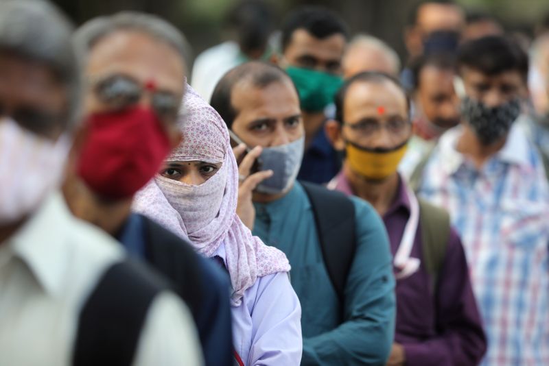 People wearing protective masks wait in line to board a