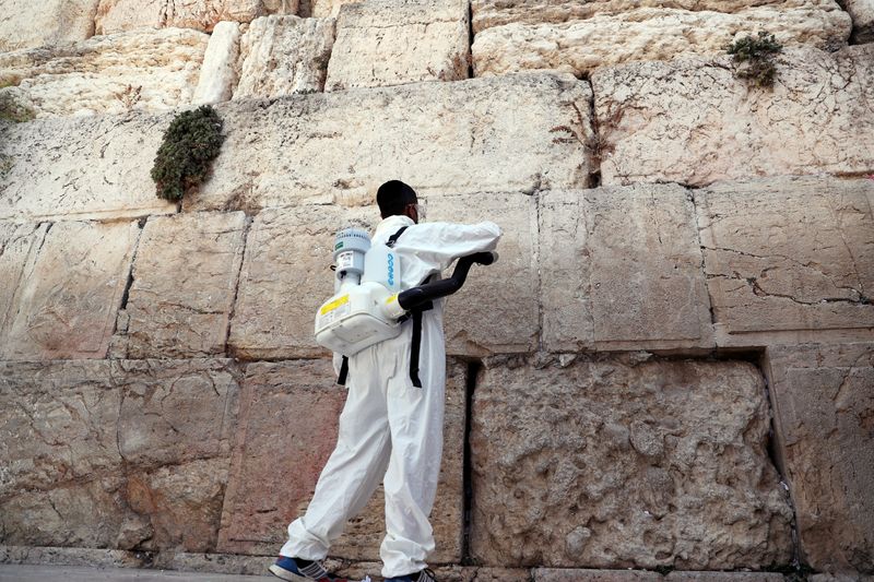 A labourer disinfects as he clears notes from Western Wall