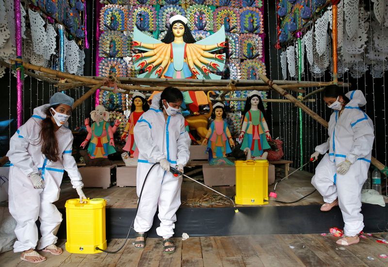Women wearing personal protective equipment sanitize a “pandal” ahead of