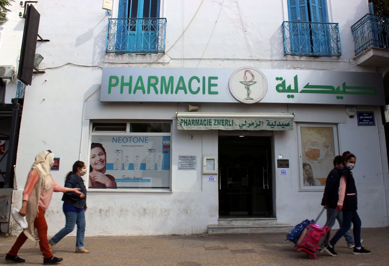 People wearing masks walk past a pharmacy in Tunis