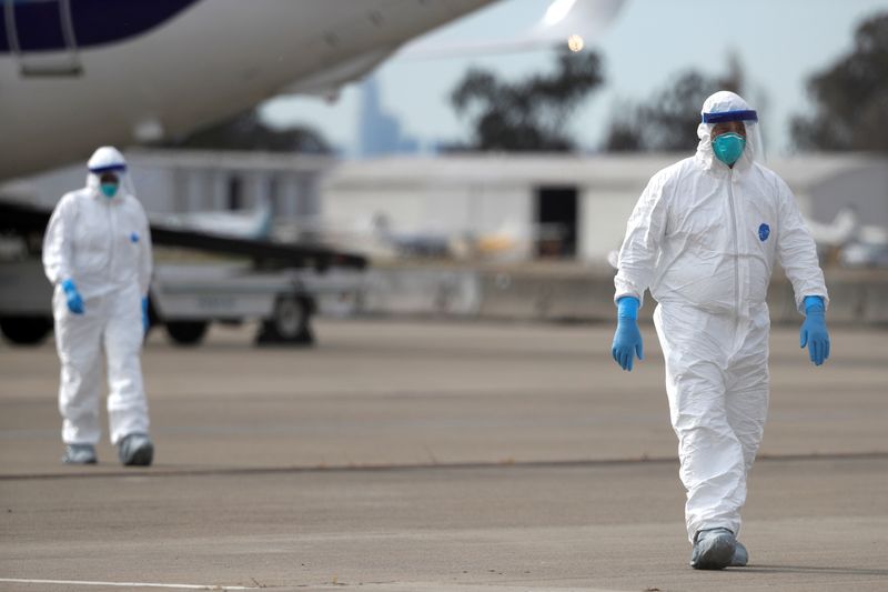 Workers in protective gear walk on the tarmac at Oakland