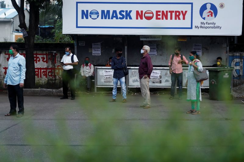 People wearing protective masks wait at a bus stop amidst