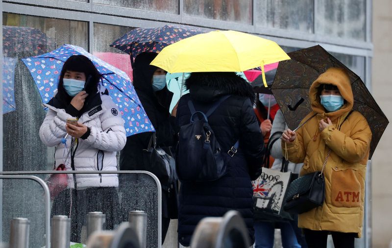 FILE PHOTO: People wearing face masks shelter under umbrellas outside