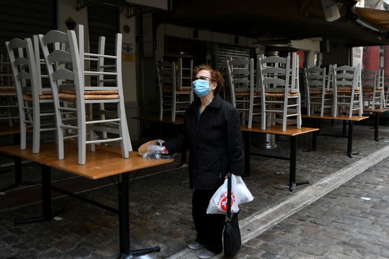 A woman stands outside a closed restaurant, amid the coronavirus
