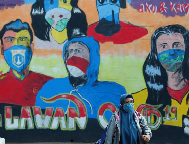 A woman wearing a protective face walks past a mural