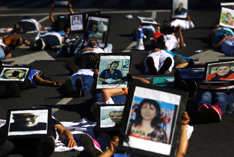 Health workers lie on the floor while holding photographs of