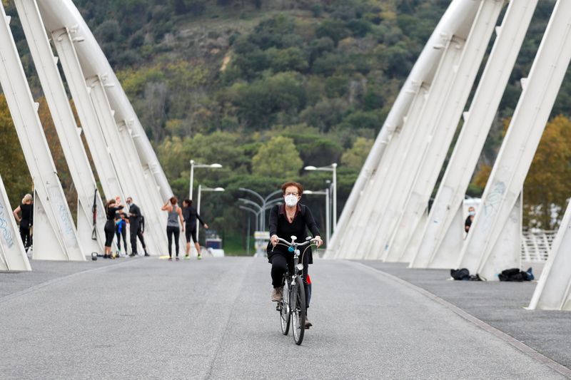 A woman wearing a protective mask cycles on Ponte della