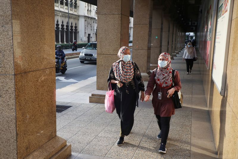 People wearing protective masks walk on a street, amid the