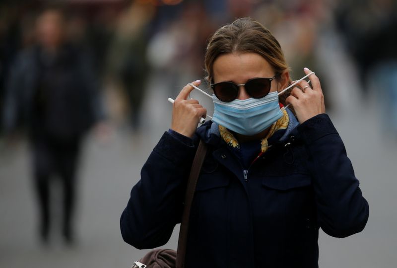 A woman adjusts her protective face mask as she walks