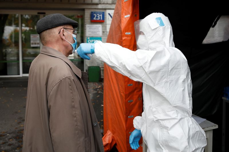 A man in protective suit checks a man’s temperature in