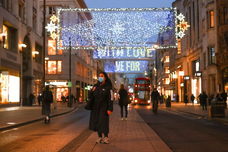 A pedestrian wearing a face mask stands under Christmas lights