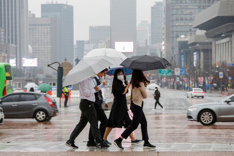 Pedestrians wearing masks walk with umbrellas as it rains amid
