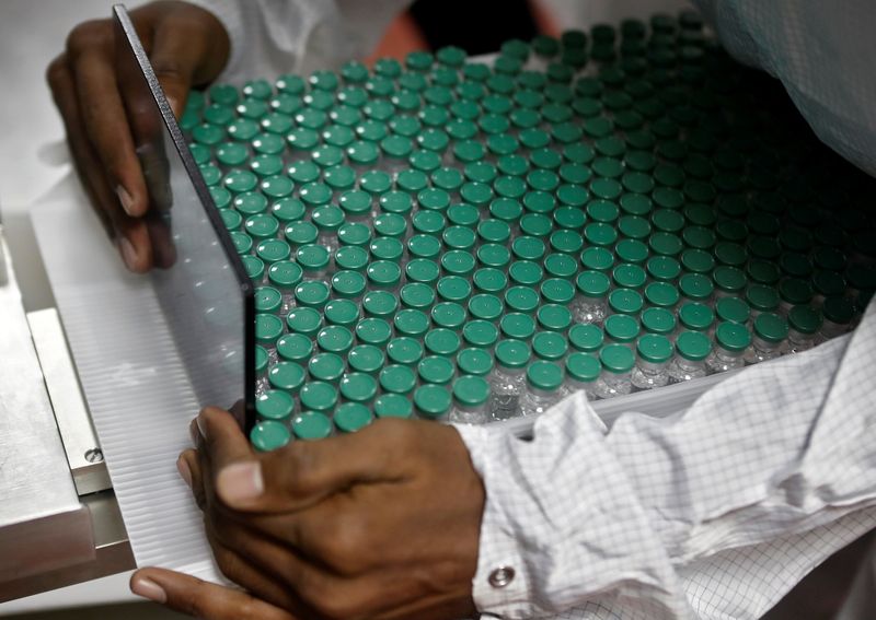 An employee in personal protective equipment (PPE) removes vials of