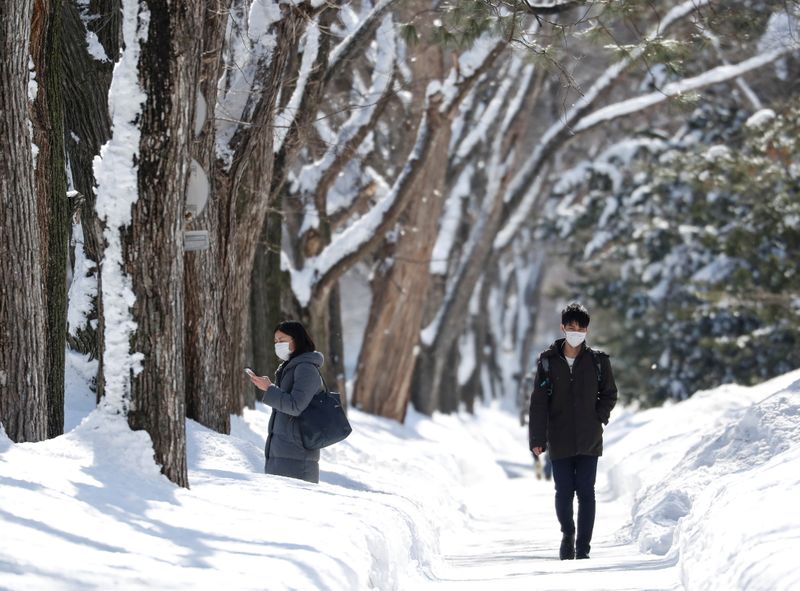 Passersby wearing protective masks walk on a snow-covered street in