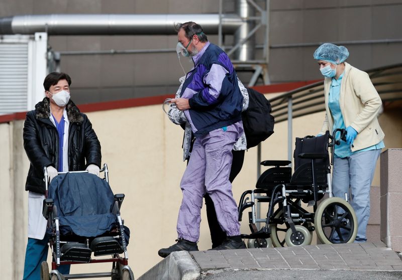 A patient wears an oxygen mask outside a hospital for