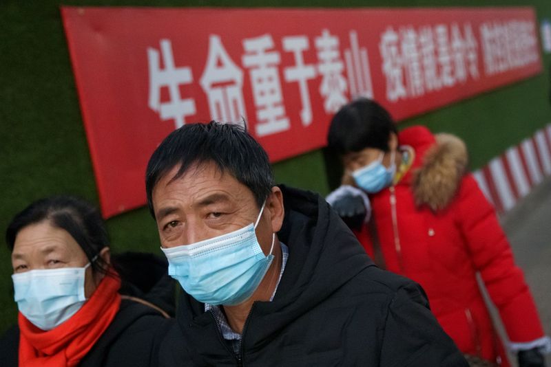 People wear face masks as they walk past a slogan