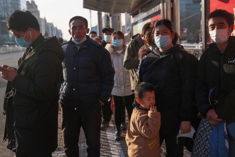 People wear face masks as they wait at a bus