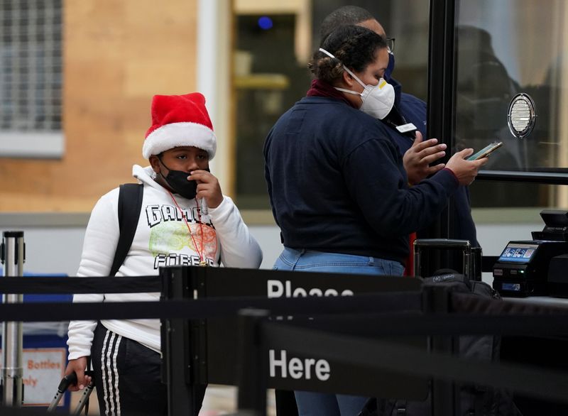 A boy wearing a Christmas hat pulls his mask up