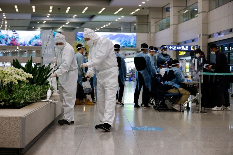 Workers wearing protective gear disinfect an arrival gate as other