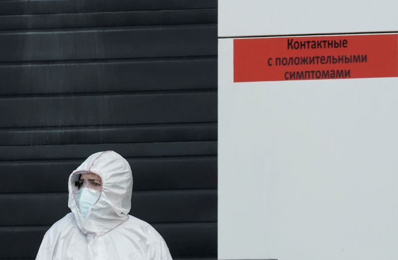 A medical specialist wearing protective gear stands outside a hospital