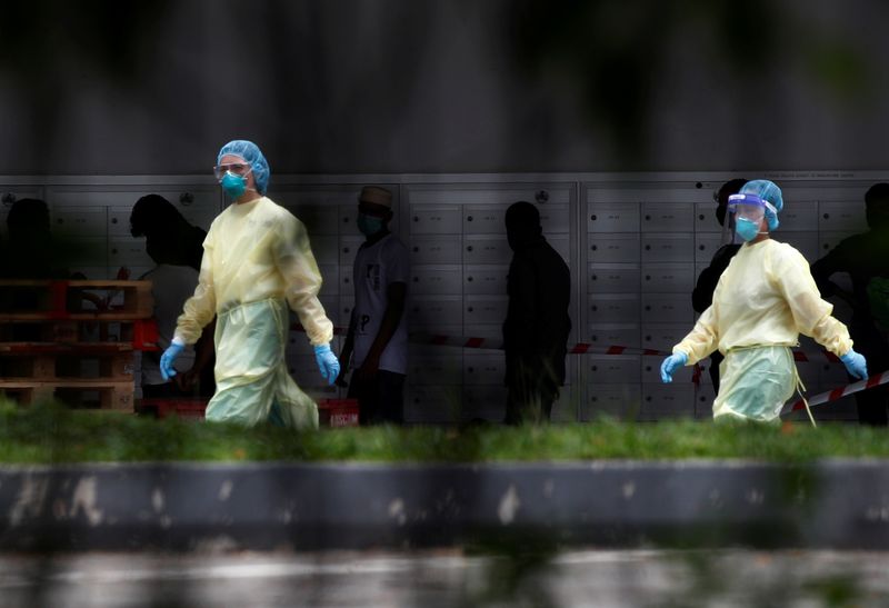 Medical personnel walk past migrant workers at a dormitory during