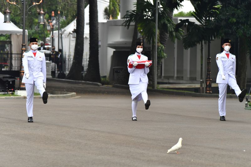 Flag bearers wearing protective masks carry Indonesia’s national flag during