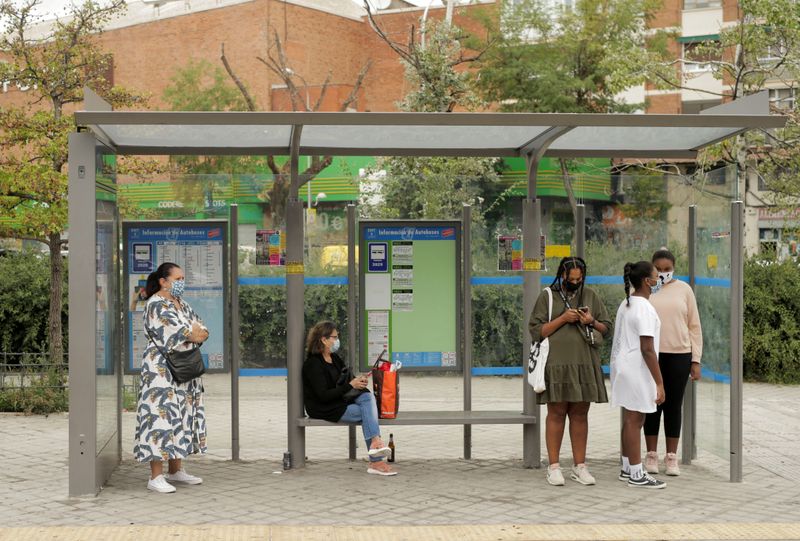 People wearing protective face masks wait at a bus stop