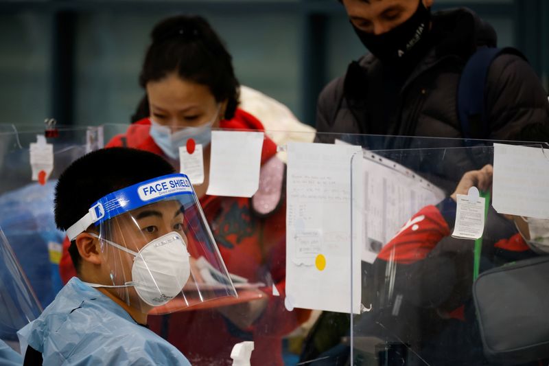 A worker wearing protective gear checks passengers from overseas as