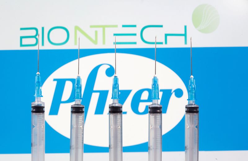 Syringes are seen in front of displayed Biontech and Pfizer