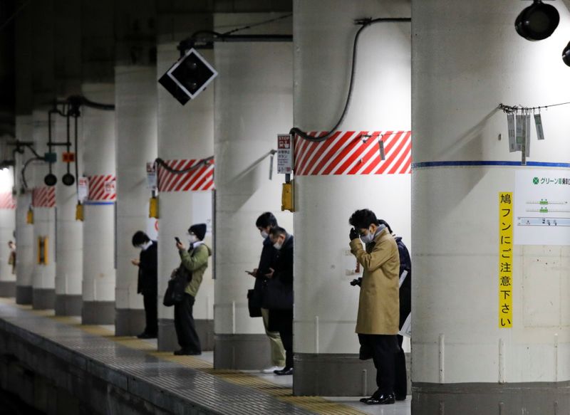 Commuters wearing protective face masks wait for arrival of a
