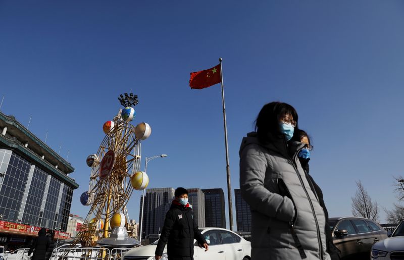 People wearing face masks walk past a Chinese flag, following