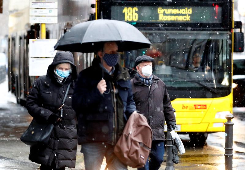 People wear face masks as they walk past a bus